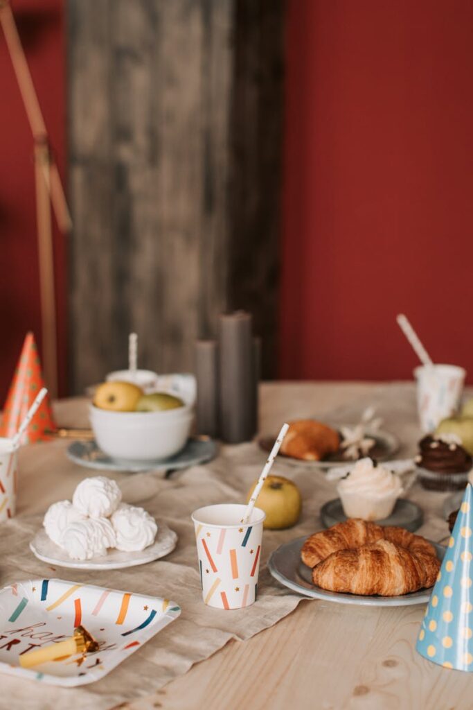 A festive table arrangement featuring croissants, meringue, apples, and party decor.