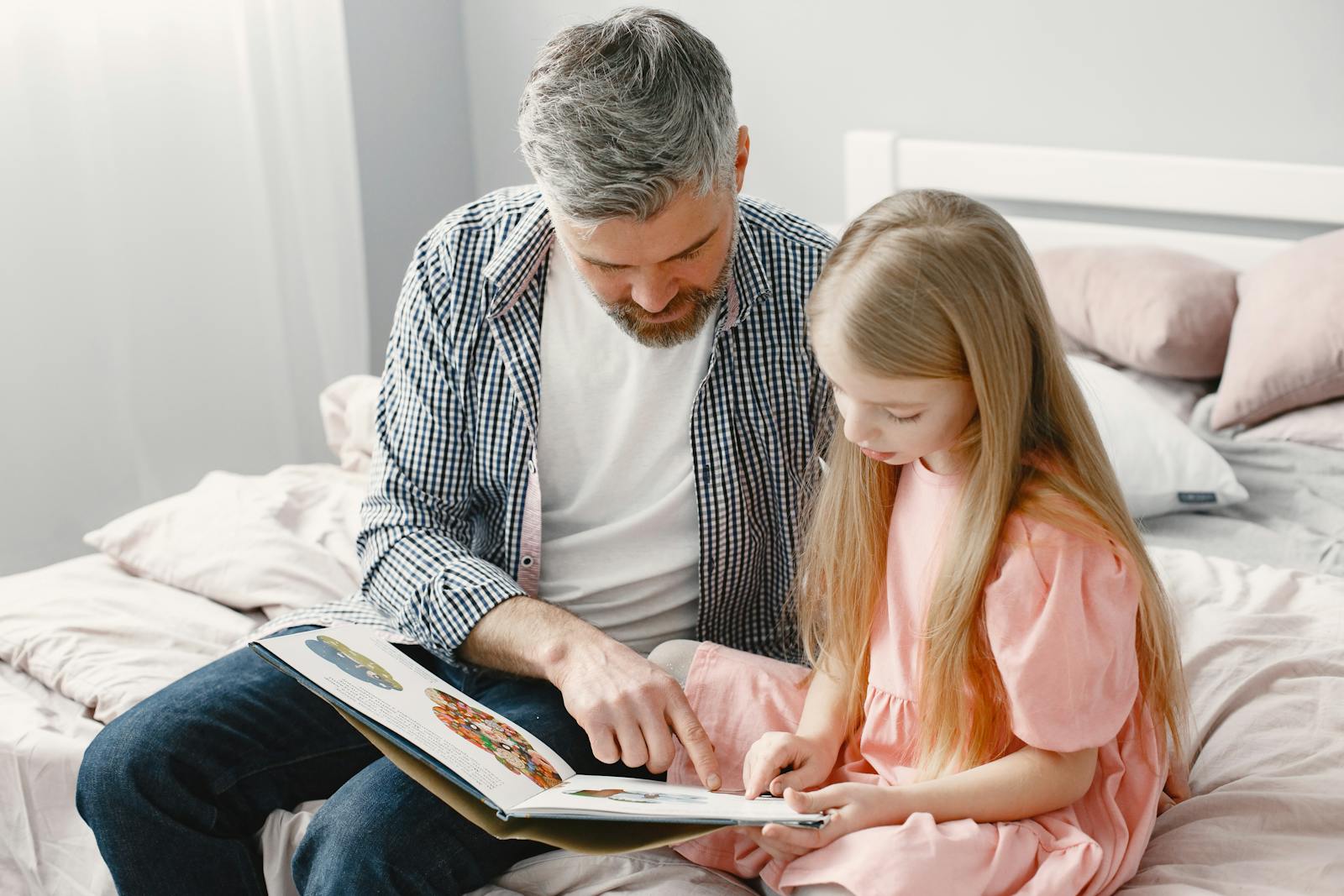 A grandfather reading a picture book with his granddaughter on a cozy bed at home.