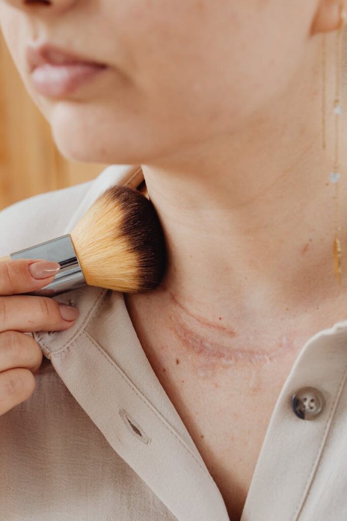 Close-up of a person using a brush to apply makeup on a neck scar, showcasing a personal care routine.