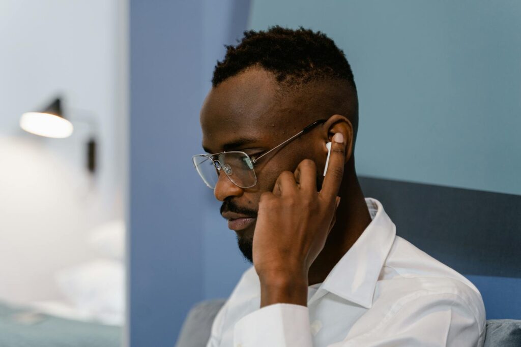 Man using earbuds in a home office setting, focusing on work tasks.