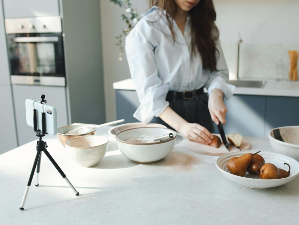 Woman slicing bosc pears in a modern kitchen, capturing the process on smartphone.