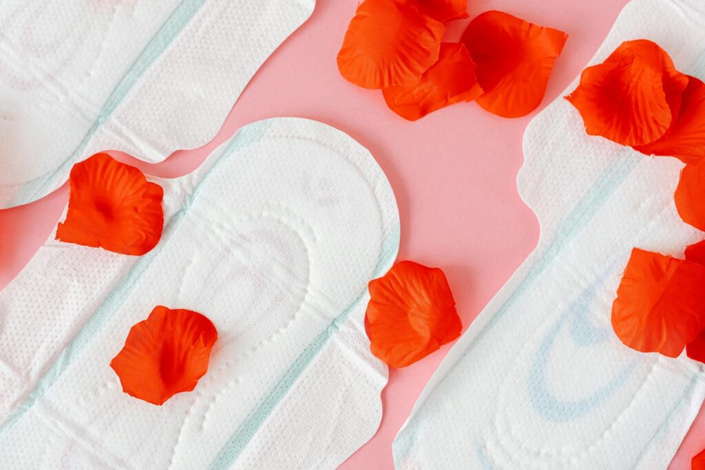 Close-up of sanitary pads with red petals on a pink background, symbolizing menstruation.