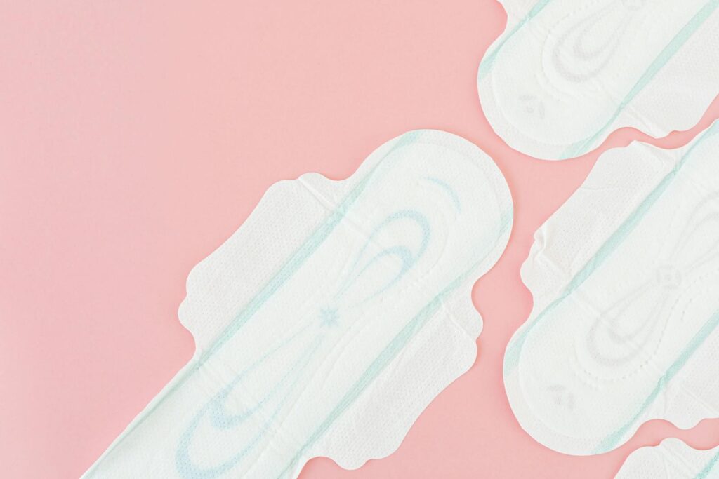 Top view of sanitary pads arranged on a light pink background with ample copy space.