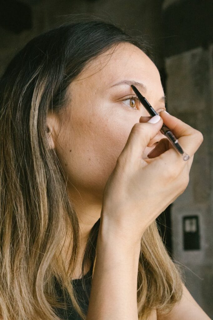 Close-up of a woman applying makeup with an eyebrow pencil indoors.