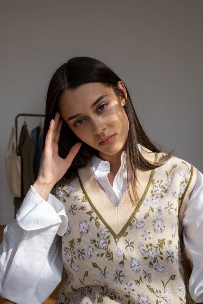 Elegant woman in a floral vest posing indoors with sunlight filtering through.