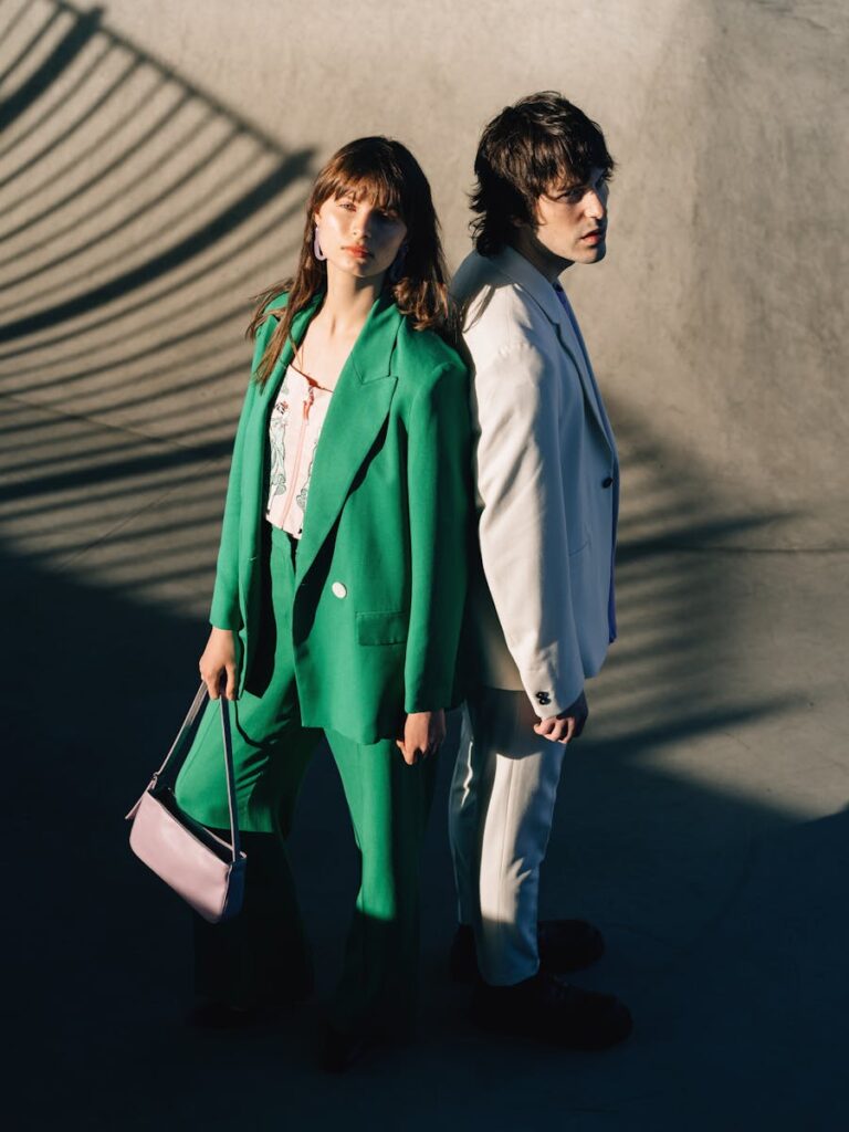 Stylish couple in vibrant suits posing back to back in outdoor sunlight.