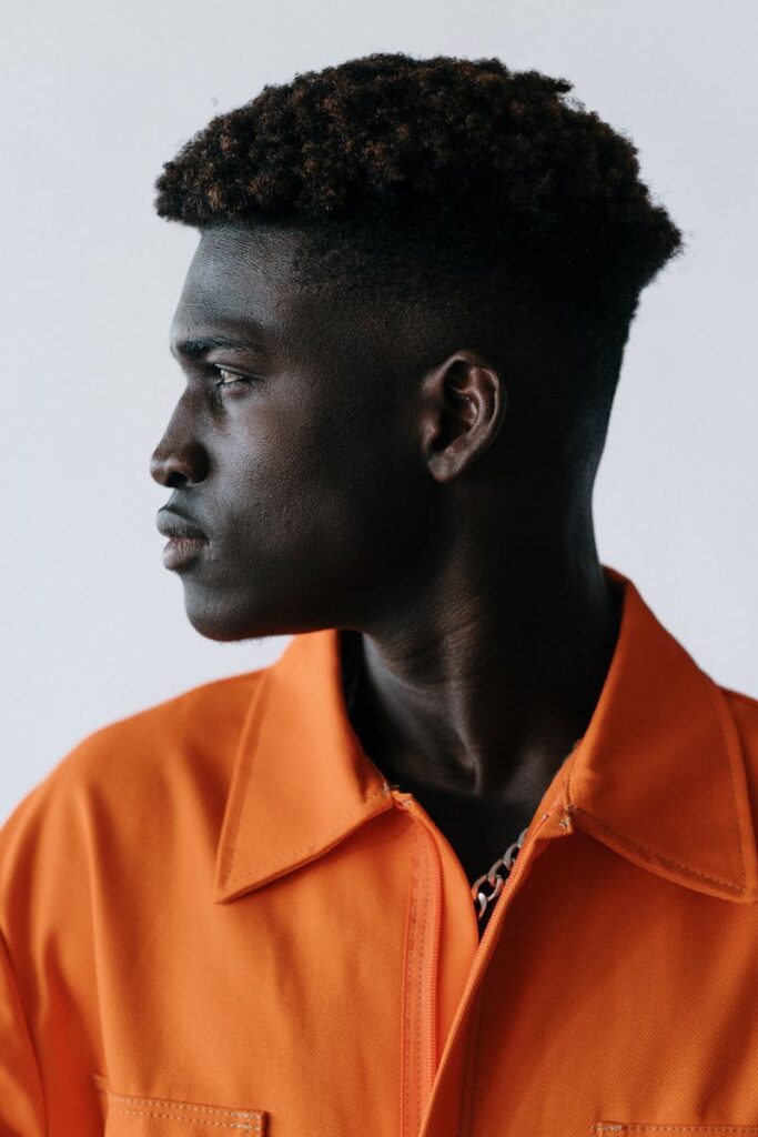 Side profile portrait of a man in a vibrant orange jacket against a white background.
