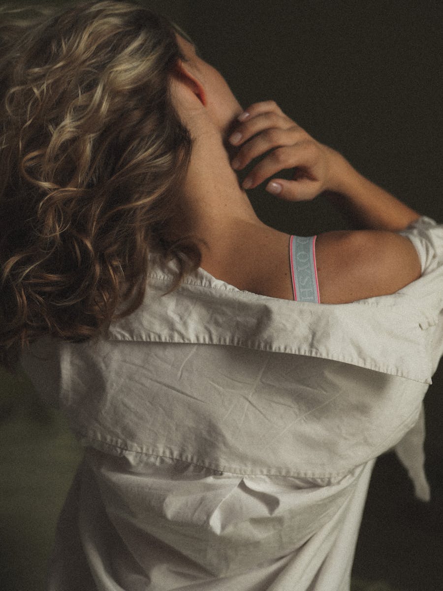 Back view of a woman with curly hair, hand on neck, creating a serene and intimate mood.
