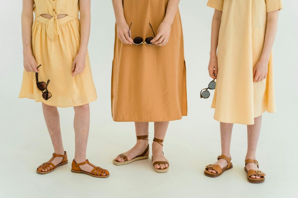 Minimalist image of three women in dresses and sandals holding sunglasses indoors.