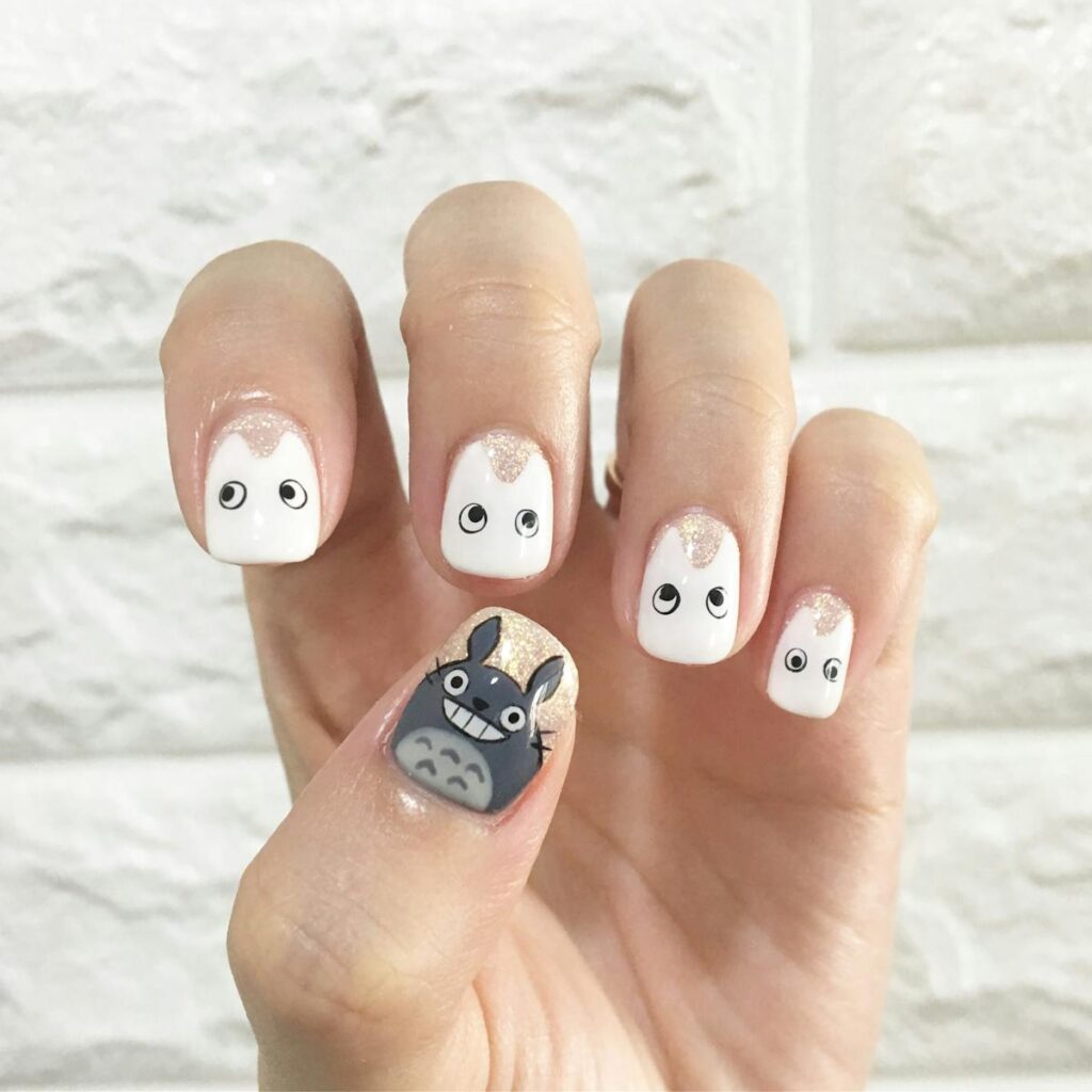 Charming Totoro-themed nail art design featuring cute characters on manicured nails against a stone wall background.