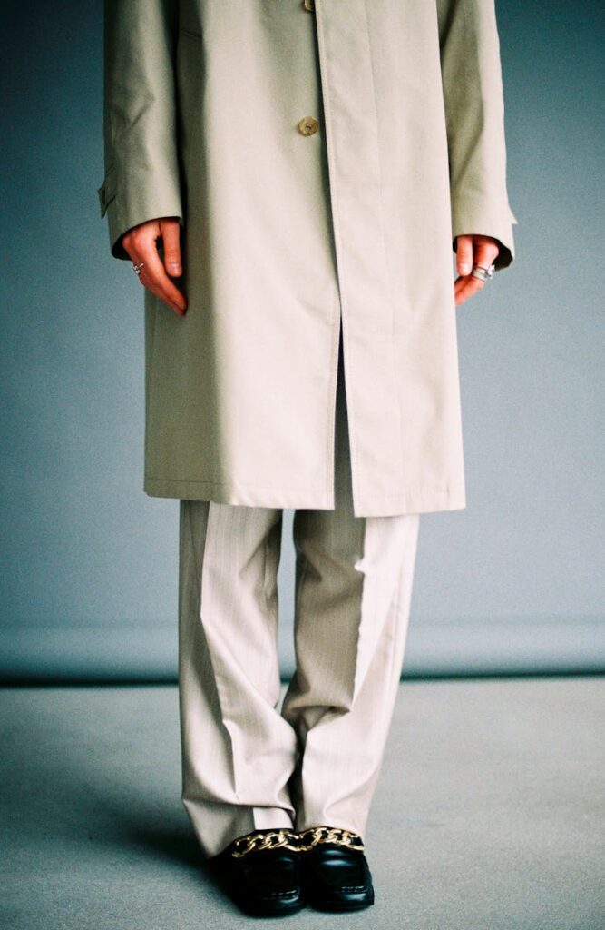 Stylish studio photo of a person in a beige trench coat and pants with chain loafers, exuding elegance.