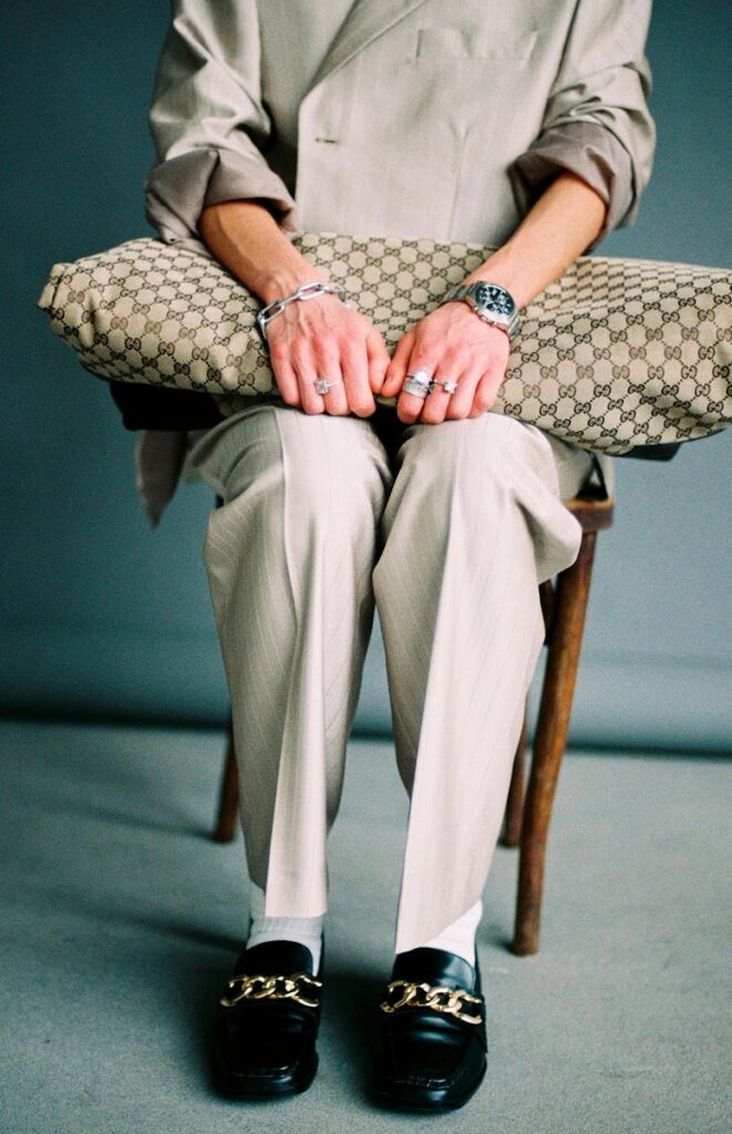 Stylish man in beige suit and loafers holding a designer bag, showcasing luxury fashion accessories.
