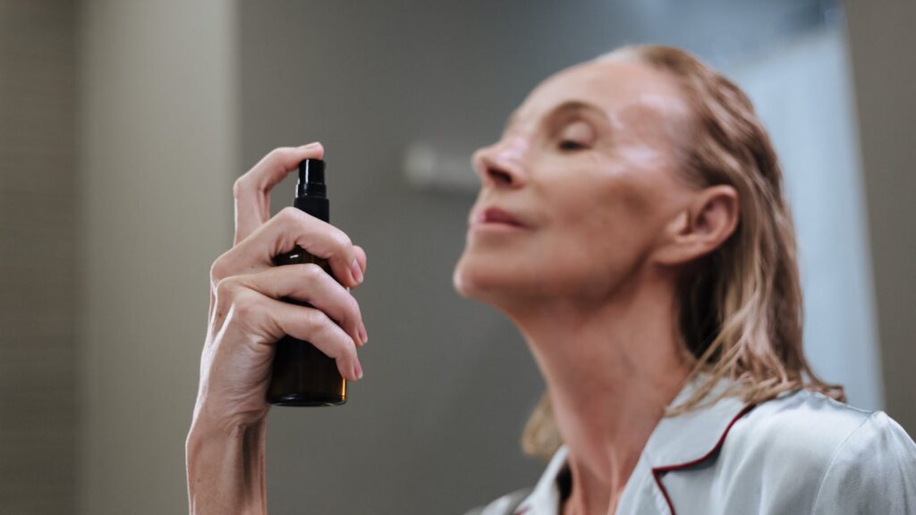 Senior woman demonstrating daily skincare routine, spraying face with a beauty product.