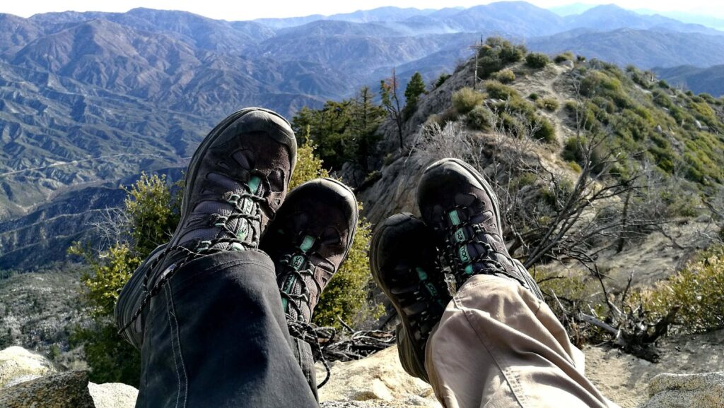 Two hikers resting with boots in view, overlooking a scenic mountain landscape.
