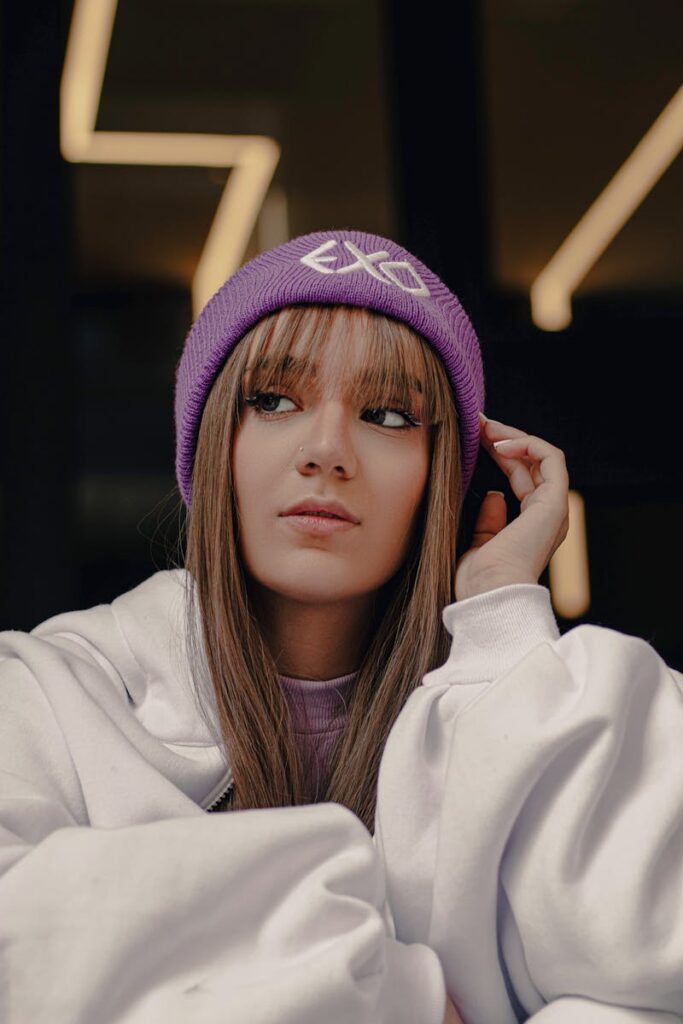 Stylish young woman wearing a purple beanie and white hoodie indoors, showcasing fashion and modern vibes.