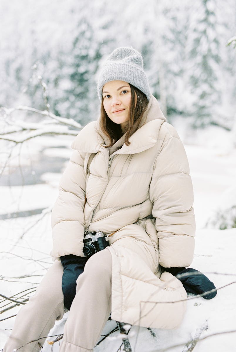 Woman in warm clothing sitting in a snowy forest, captured during winter.