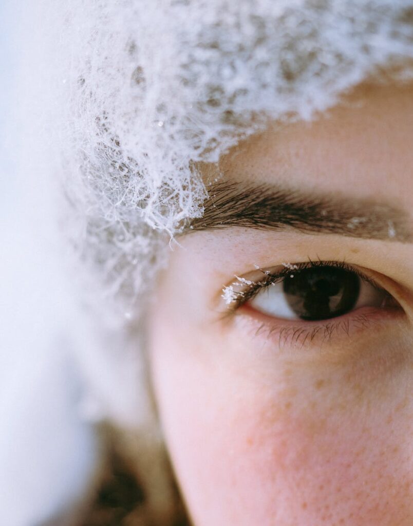 Close-up shot of a woman's eye in winter, with snow-covered hat and frost.