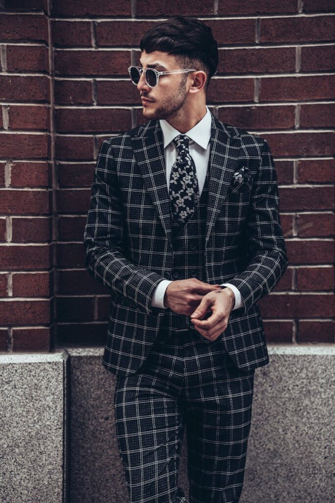 Man in plaid suit with sunglasses leaning against a brick wall in Istanbul.