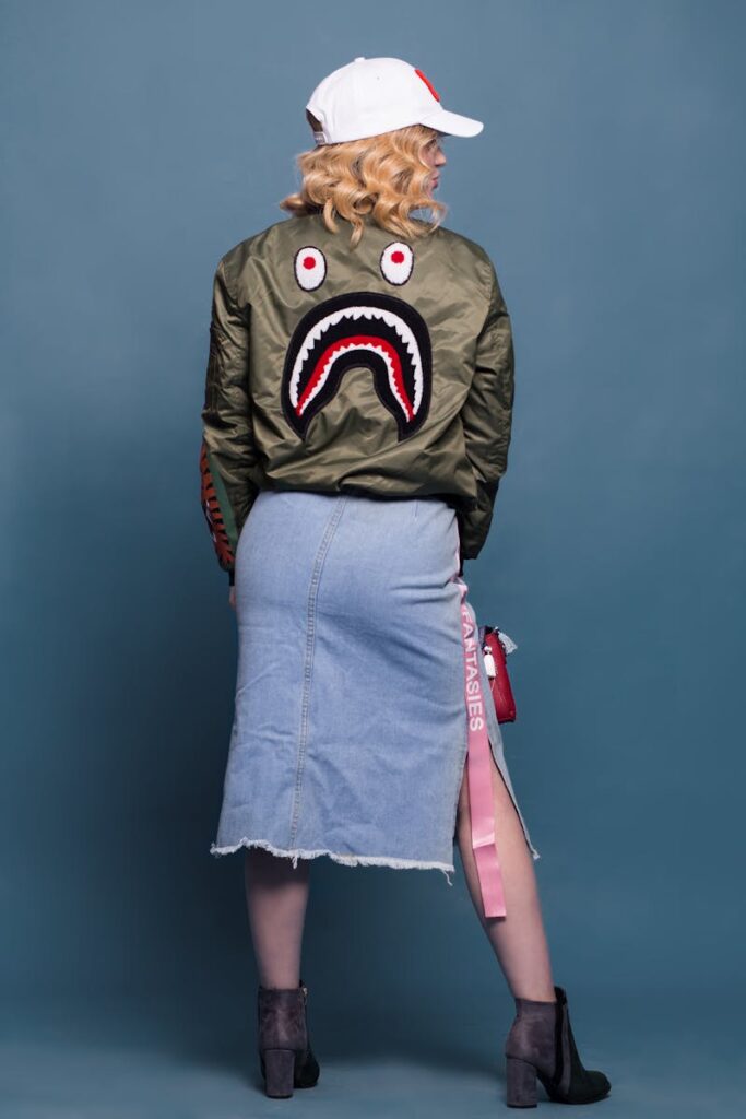 Stylish photoshoot of a woman wearing a unique bomber jacket with denim skirt and cap in studio.