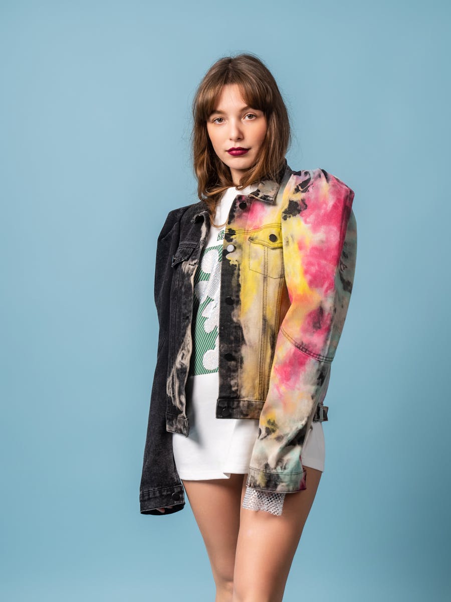 Fashionable woman wearing a colorful jacket, posing confidently against a blue background.