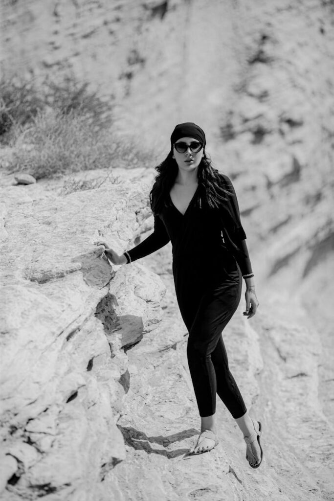 Black and white photo of a woman in a headscarf walking on a rocky cliff outdoors.