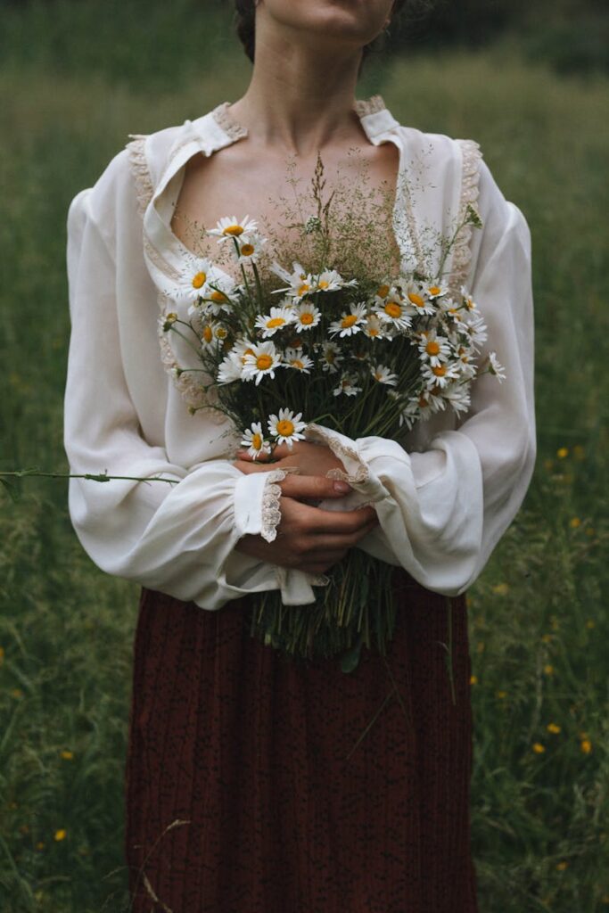A woman in a white blouse holds a daisy bouquet in a serene summer meadow.