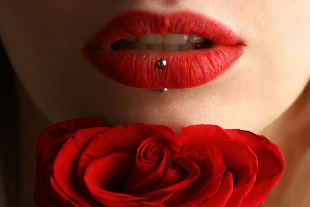 Aesthetic close-up featuring red lipstick, lip piercing, and a red rose.