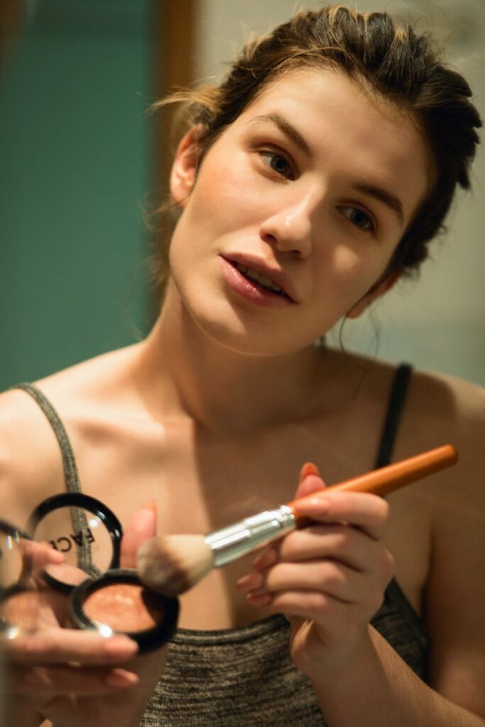 Young woman applying makeup using a brush, focusing on smooth skin and healthy complexion.