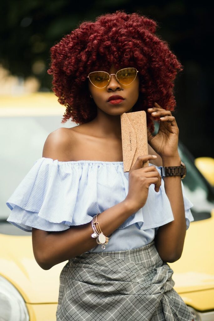 Fashionable woman with red curly hair posing outdoors in summer style