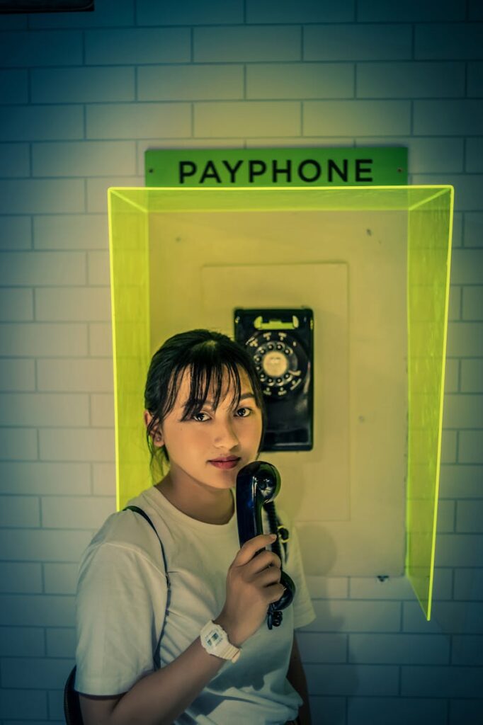 A young woman holding a payphone indoors, featuring a retro style and unique ambiance.