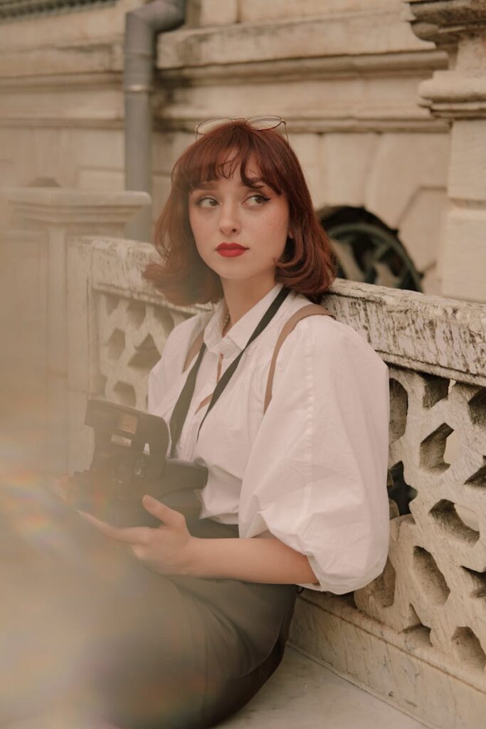 Charming portrait of a redhead woman with retro style holding a camera, evoking a vintage and nostalgic feel.