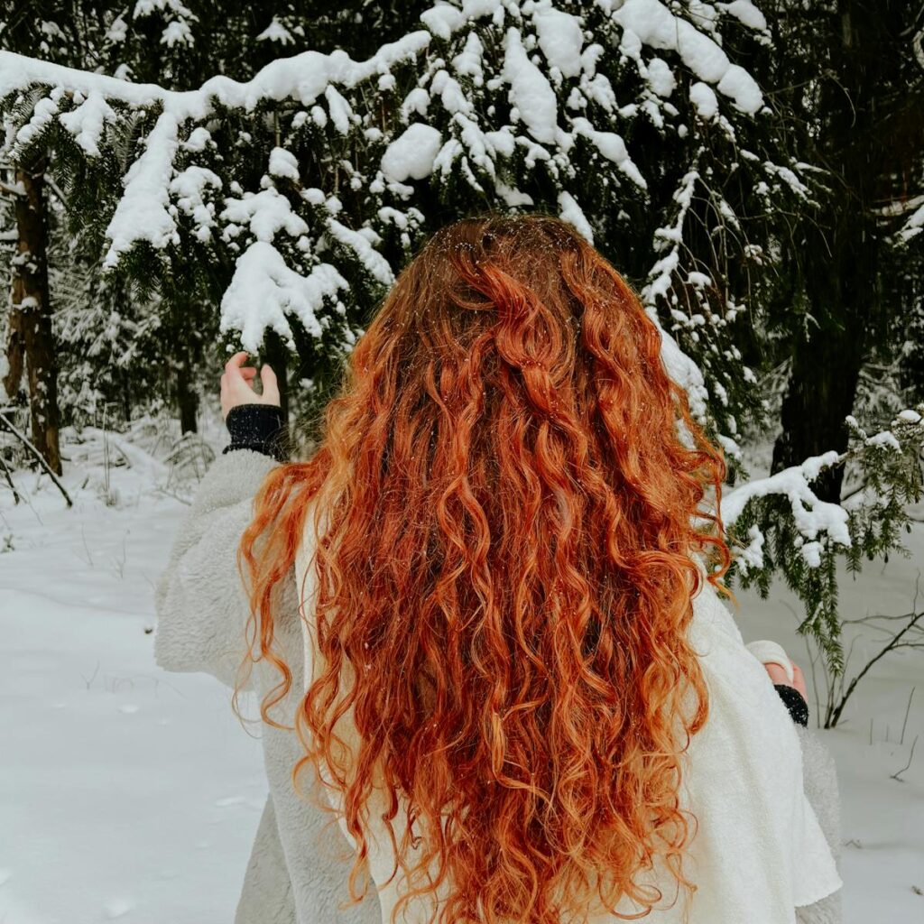 Redhead woman with curly hair in a snowy forest, capturing winter's beauty.