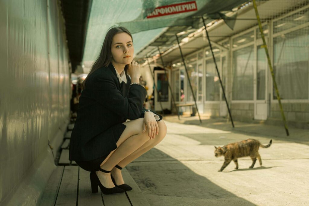 A woman in business attire crouching on a street with a cat. Urban environment captured during daytime.