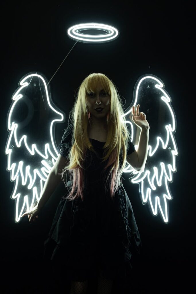 Woman in angelic costume with glowing neon wings and halo on a dark background.