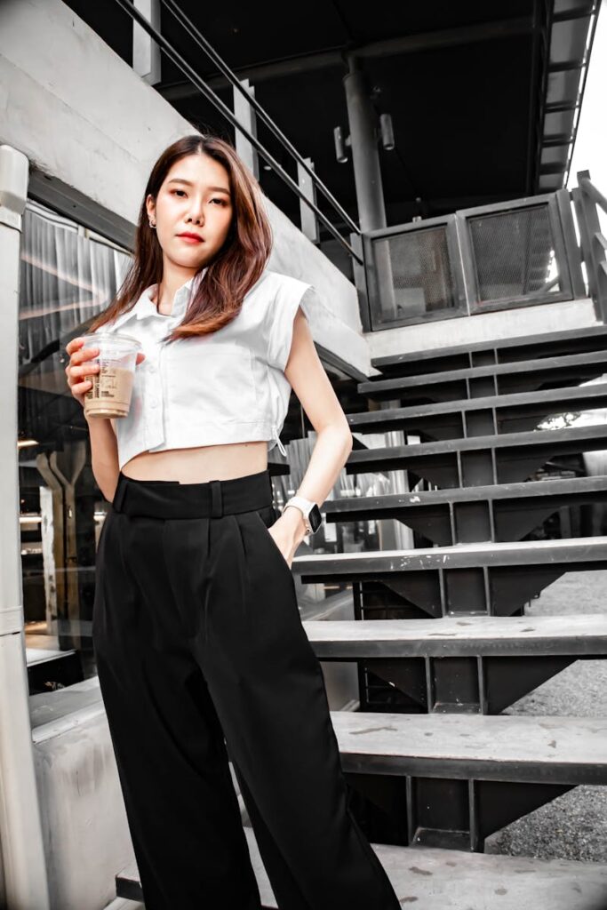 Trendy young woman holding coffee, posing in an urban outdoor setting.