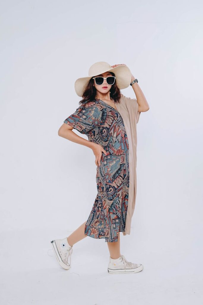 Chic woman posing confidently in stylish bohemian dress and sun hat on a neutral background.