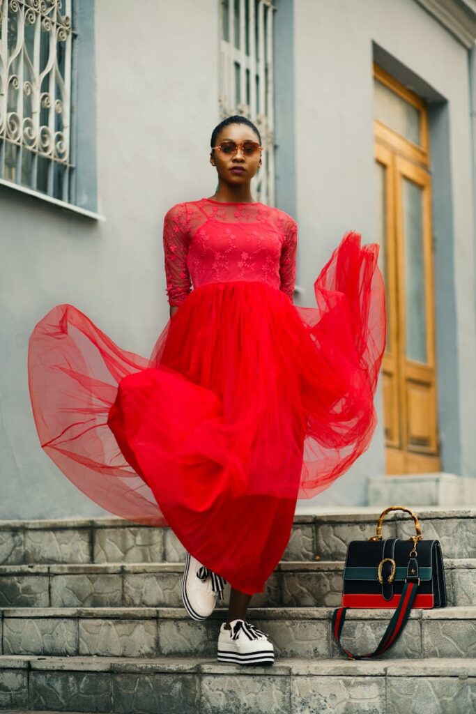 Elegant model in a red dress poses confidently on urban steps, exuding style.