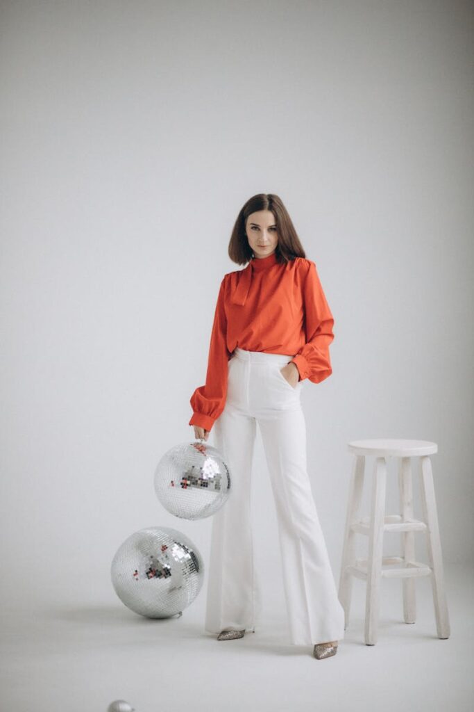 Stylish woman in orange and white attire with disco balls in a studio setting.