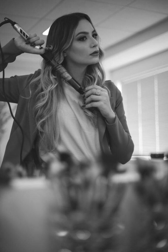Monochrome portrait of a woman using a curling iron in an indoor setting.