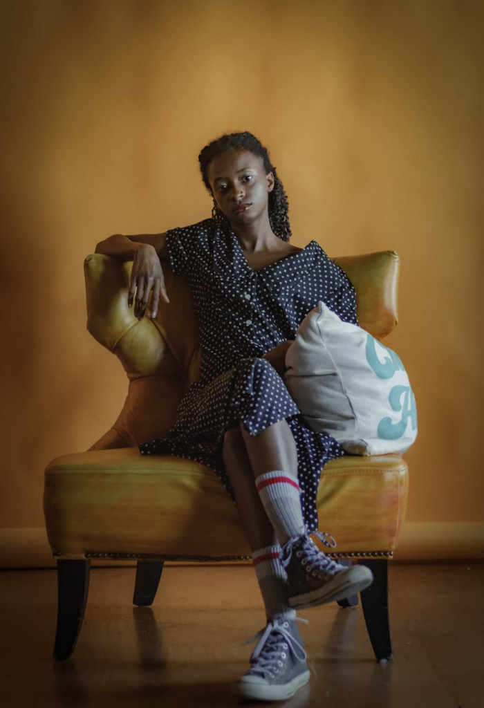 A fashionable woman in a polka dot dress sitting on a vintage armchair indoors.