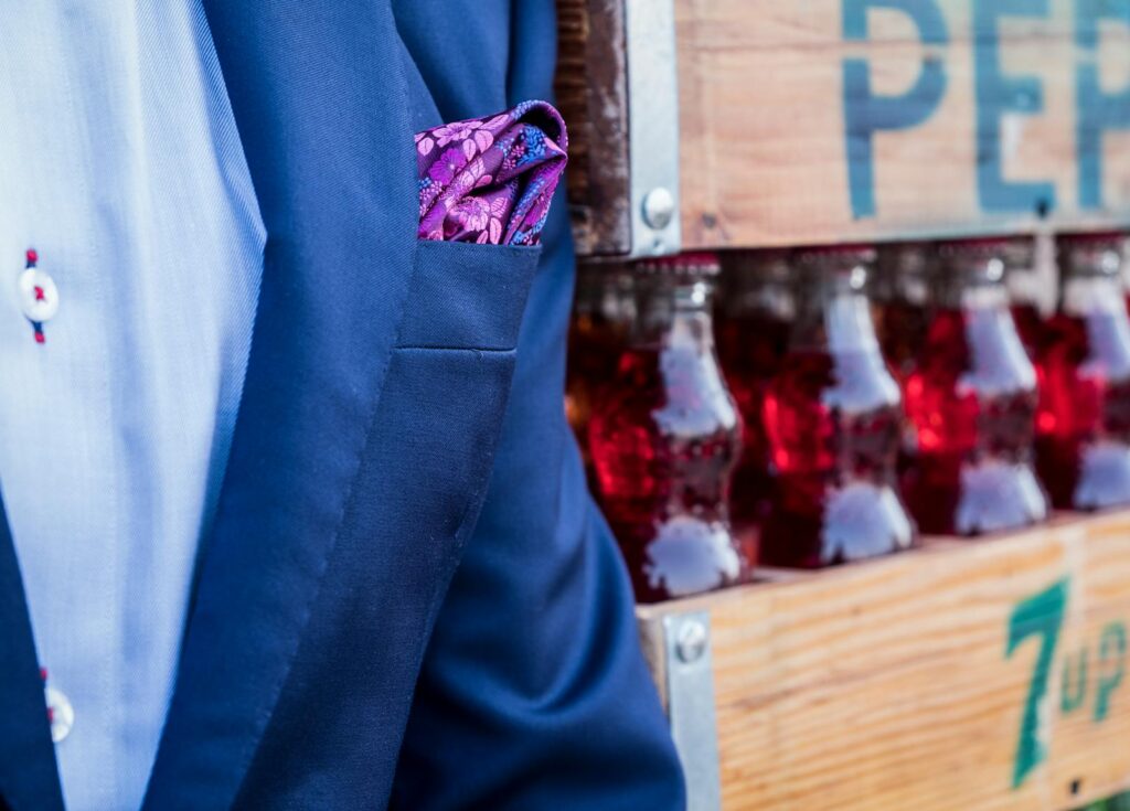 Close-up of a blue suit with a purple pocket square against a backdrop of soda bottles.