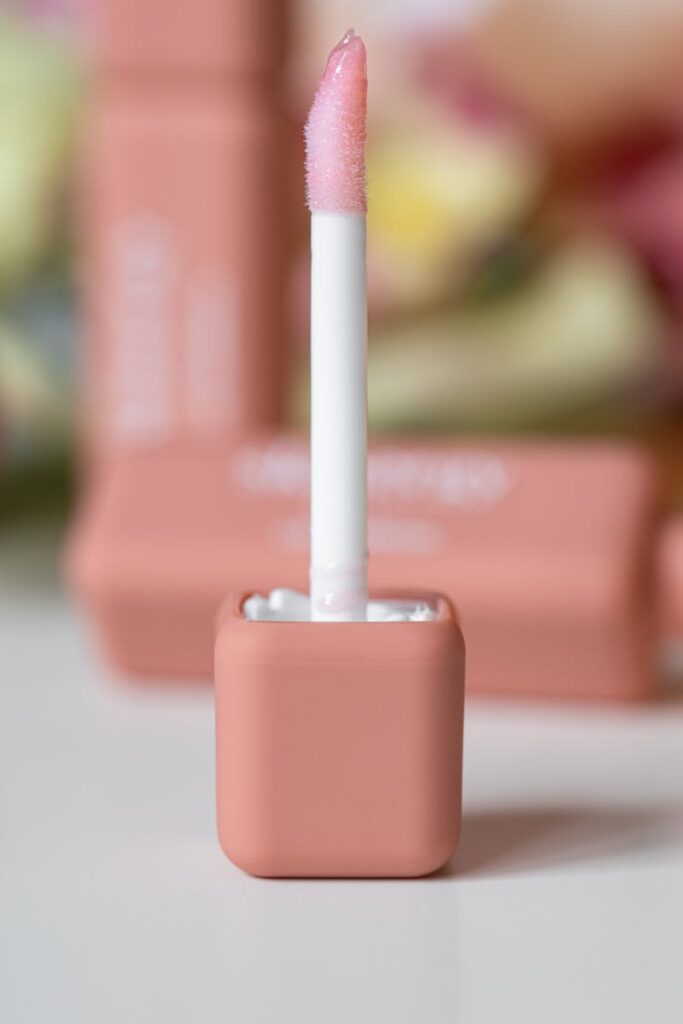 A refined close-up of a pink lip gloss applicator with soft background tones.