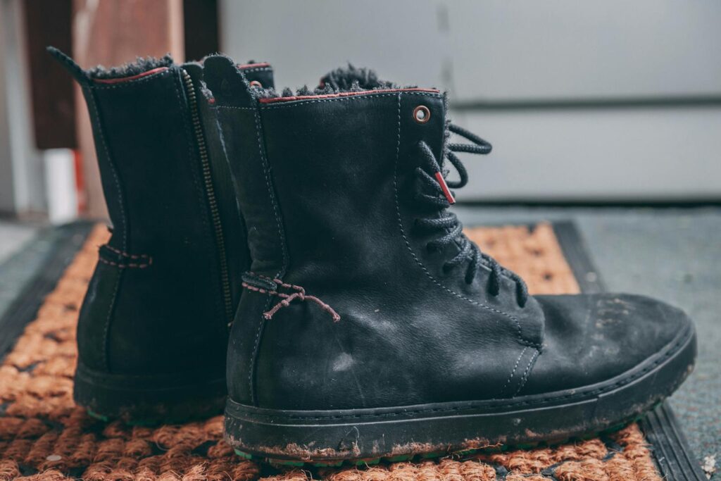 Close-up view of black leather winter hiking boots on a doormat indoors.