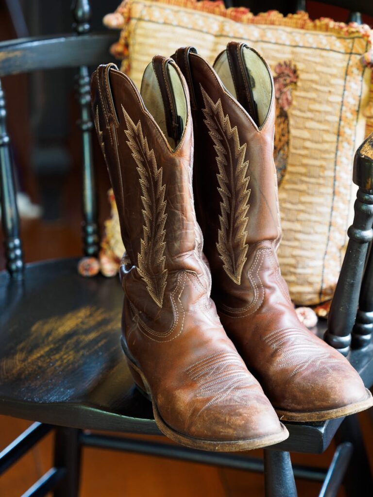 Pair of classic leather cowboy boots displayed on a rustic wooden chair indoors.