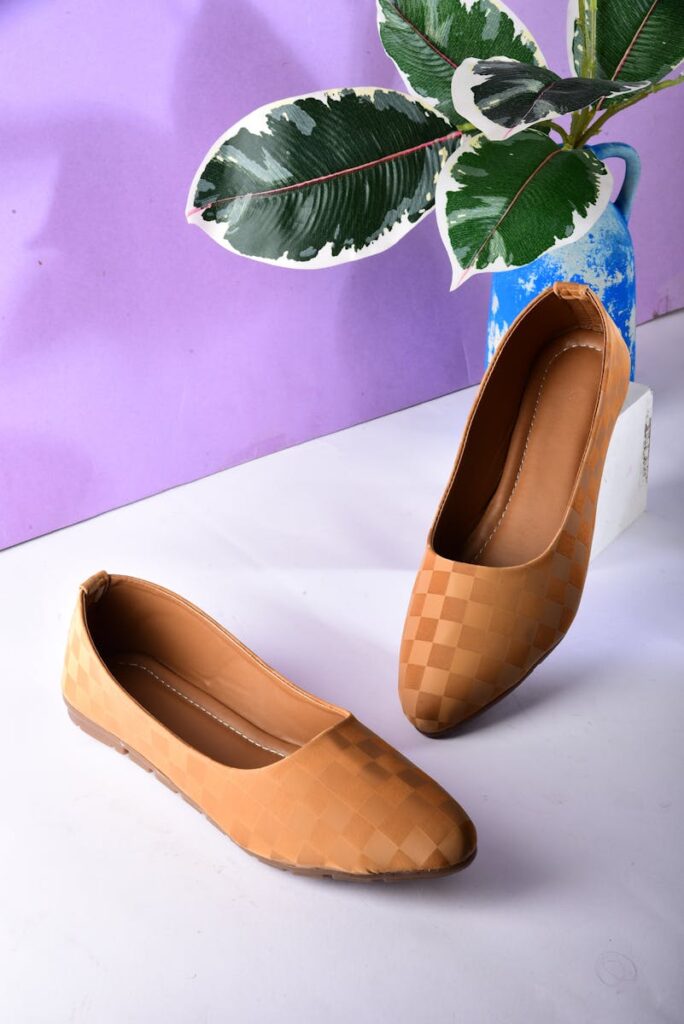 Elegant brown checkered sandals displayed on a white surface with green leaves backdrop for aesthetic appeal.