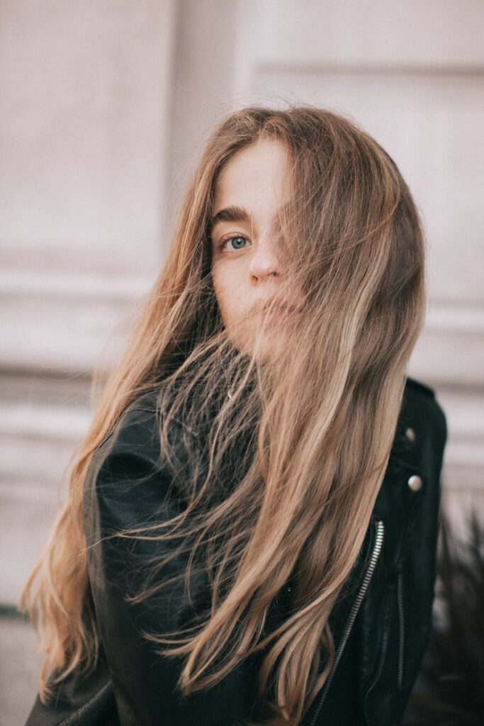 Portrait of a young woman with long hair in the wind, wearing a leather jacket outdoors.