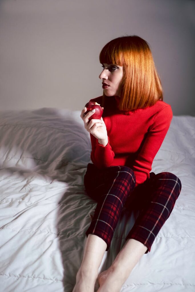 Stylish portrait of a young woman with red hair holding an apple in a bright indoor setting.