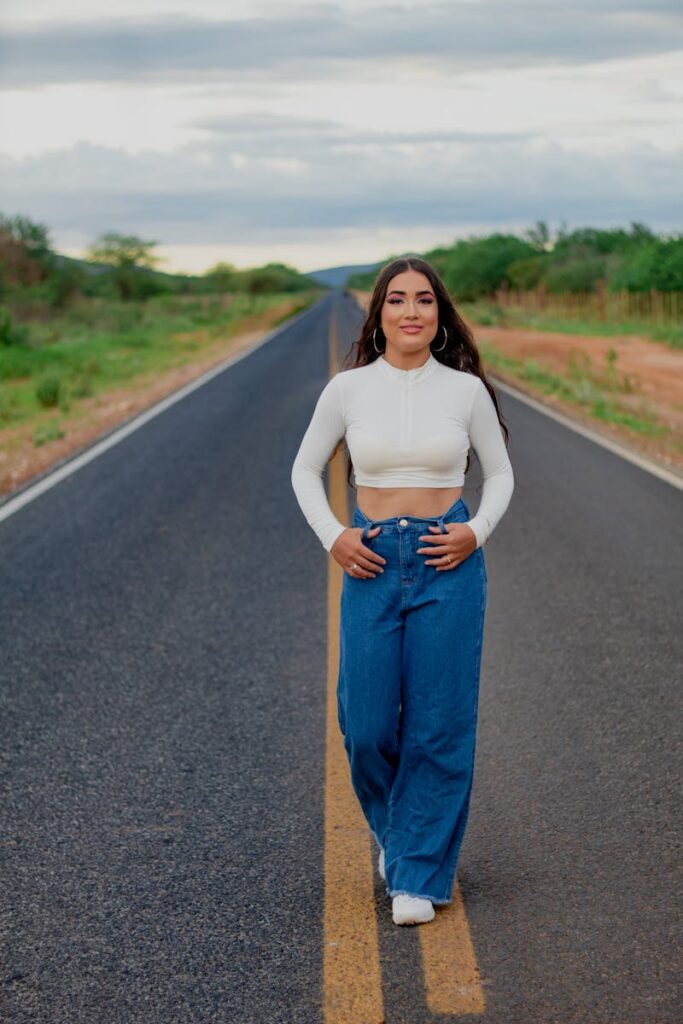 A young woman in trendy wide-leg jeans and crop top walking confidently on a rural road.