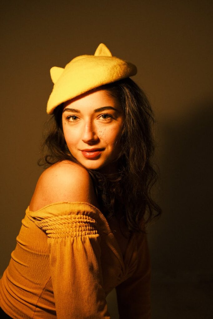 Woman posing confidently in studio, wearing a fashionable yellow hat with cat ears and yellow top.