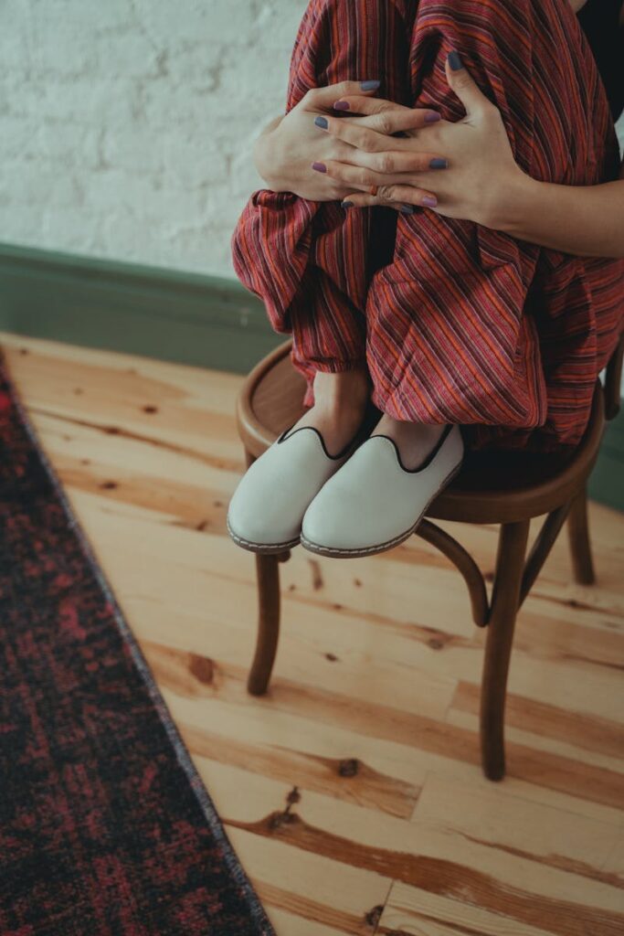 Woman in casual clothing sitting cross-legged on a chair indoors, displaying relaxed style.